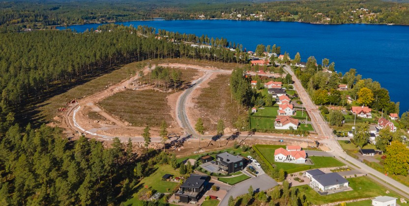 Flygfoto över ett bostadsområde vid en sjö, med skog och pågående byggarbete.