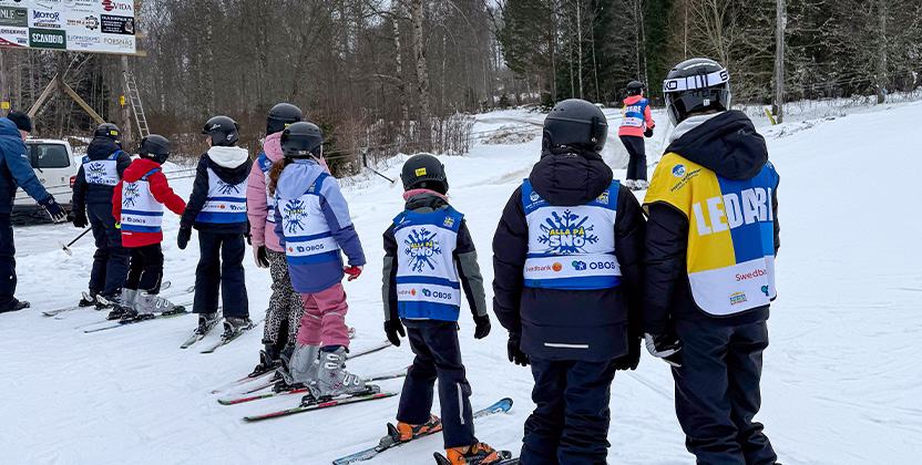 Skidlärare och barn som går i skidskola som står i kö till skidliften.