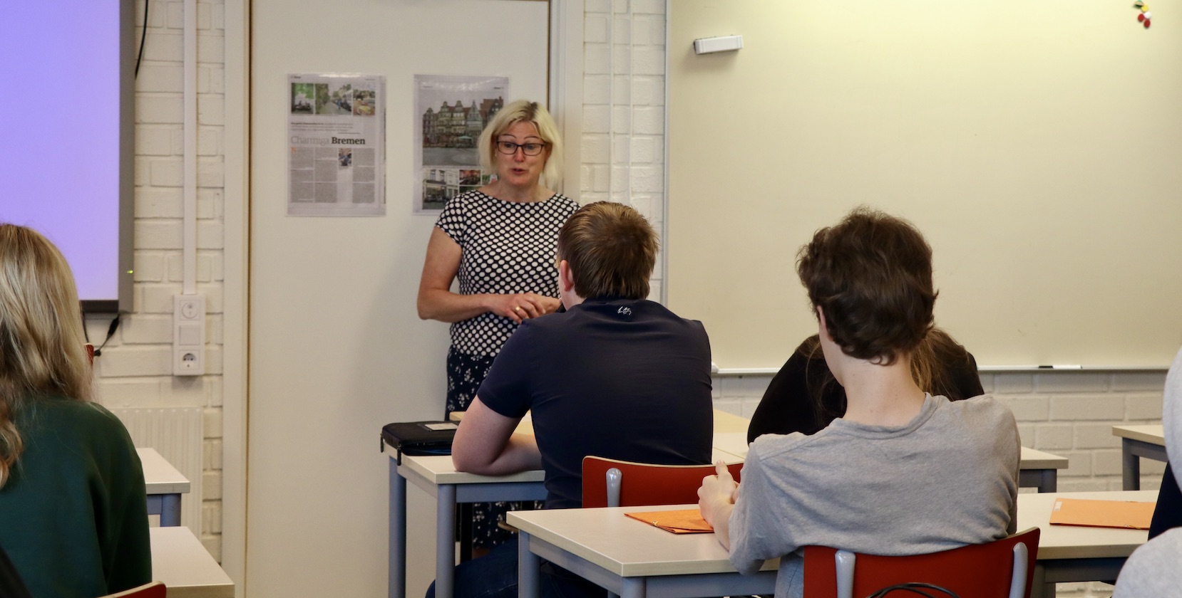 En kvinnlig lärare i medelåldern står framför en klass och presenterar. 