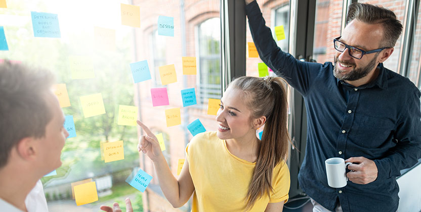 Tre personer kollar på en glasvägg med post-it lappar.