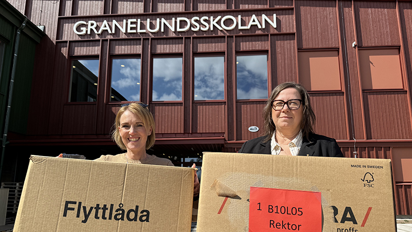 Två personer som håller varsin flyttkartong framför skolentrén.