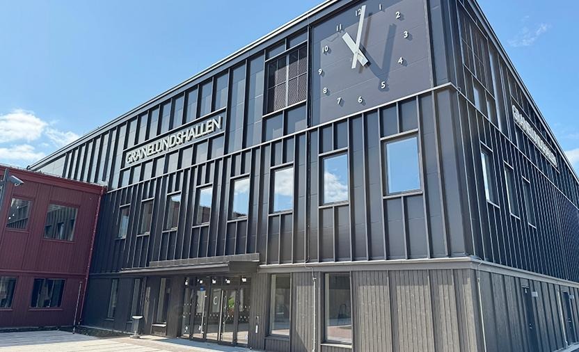 En mörk byggnad, på fasaden finns en stor klocka och en skylt med texten Granelundshallen. 