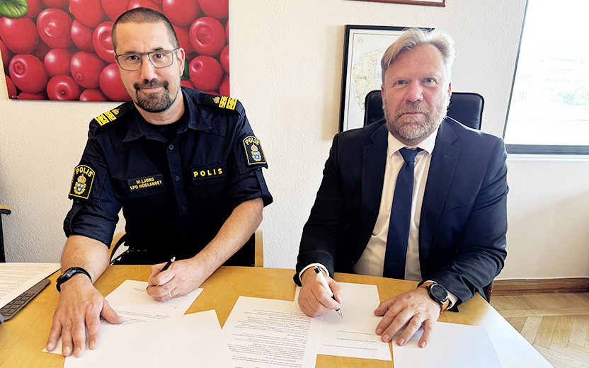 En man i polisuniform och en man i kostym signerar papper vid ett bord.