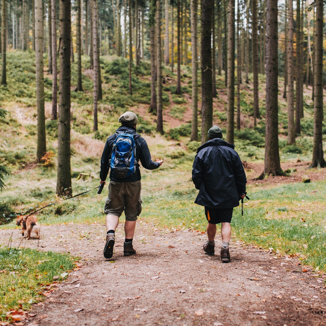 Två personer som vandrar i skogen med en hund.